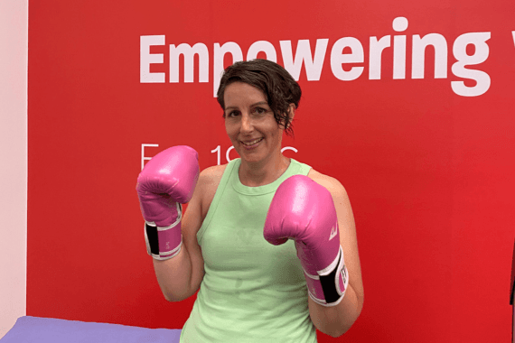 Kellie, a person living with MS is wearing pink boxing gloves and posing