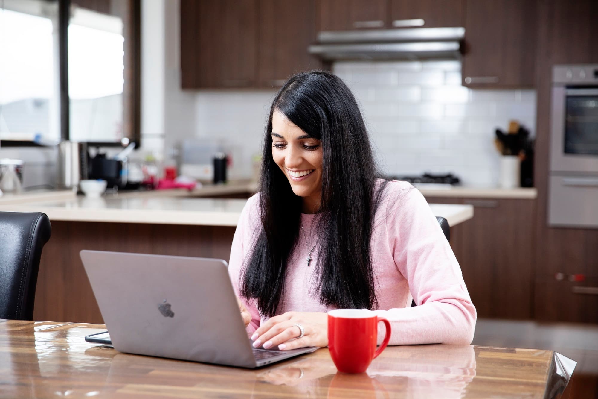 A woman seated at a kitchen table using a laptop computer.