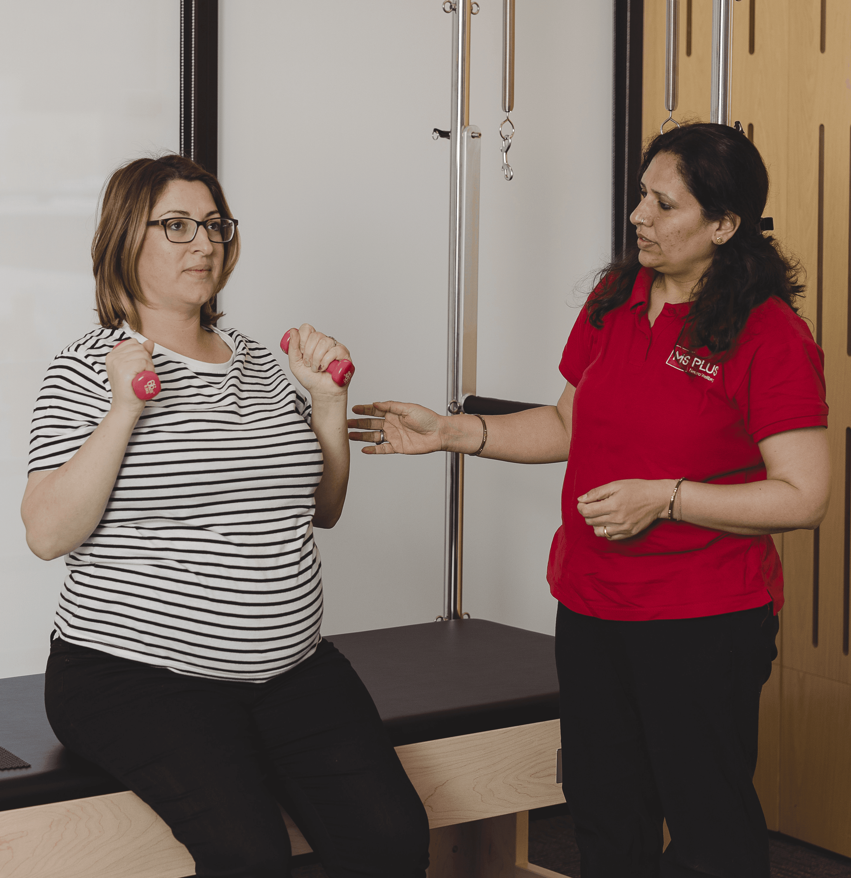 An Allied Health Assistant supporting a woman exercising with two handweights.