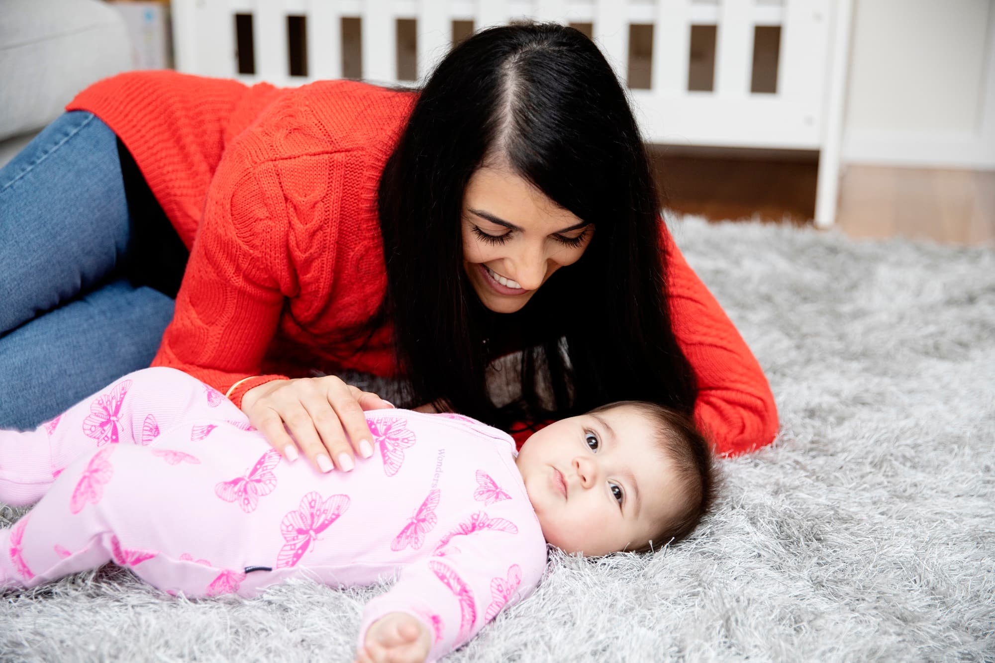 A woman lying on a rug beside a baby, with her hand on the baby's chest.
