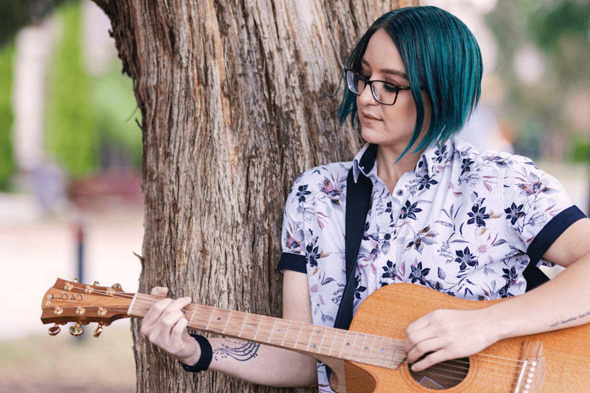 Jemma Rose leaning against a tree and playing a guitar