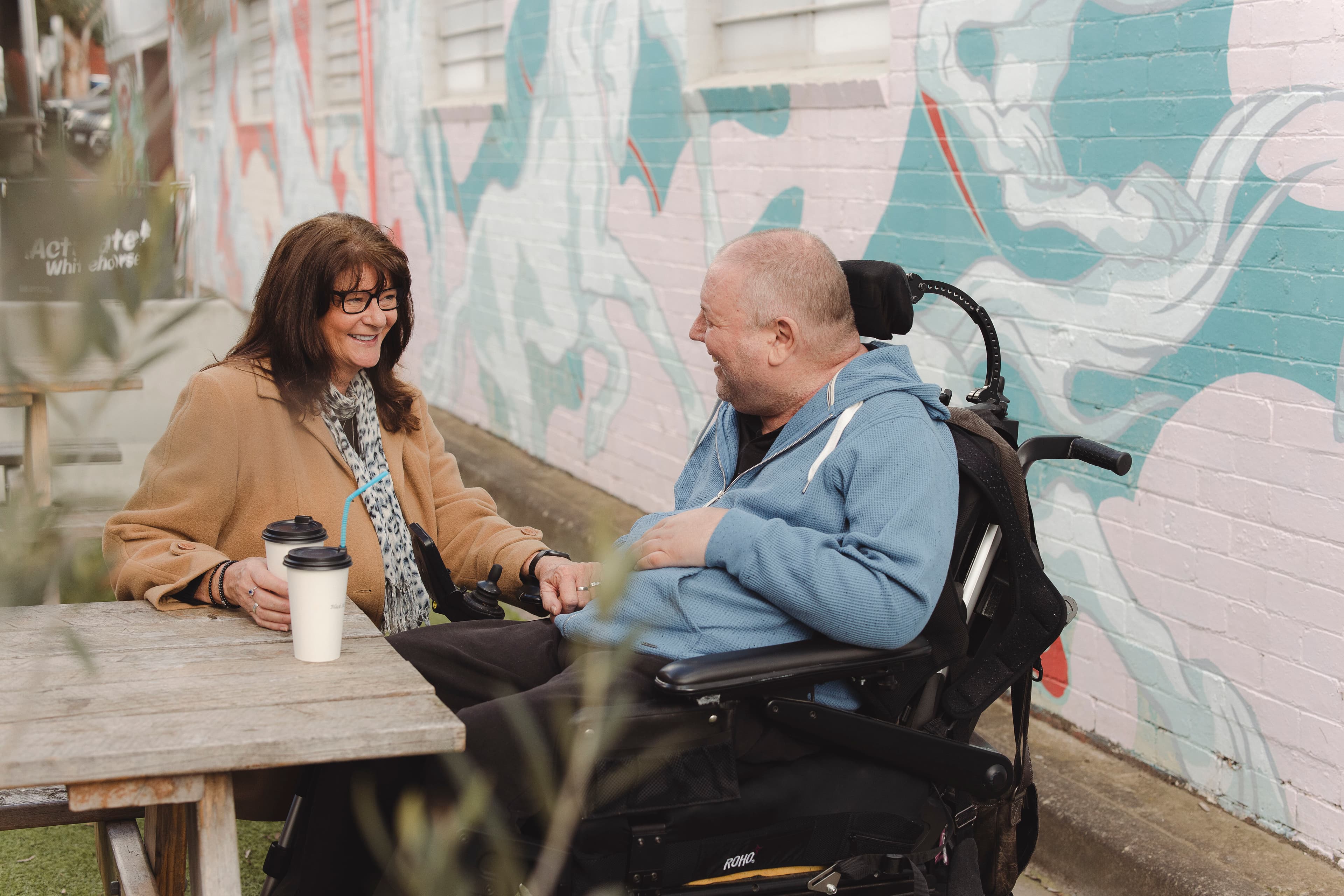 A man with multiple sclerosis seated in a wheelchair having a coffee with a woman.