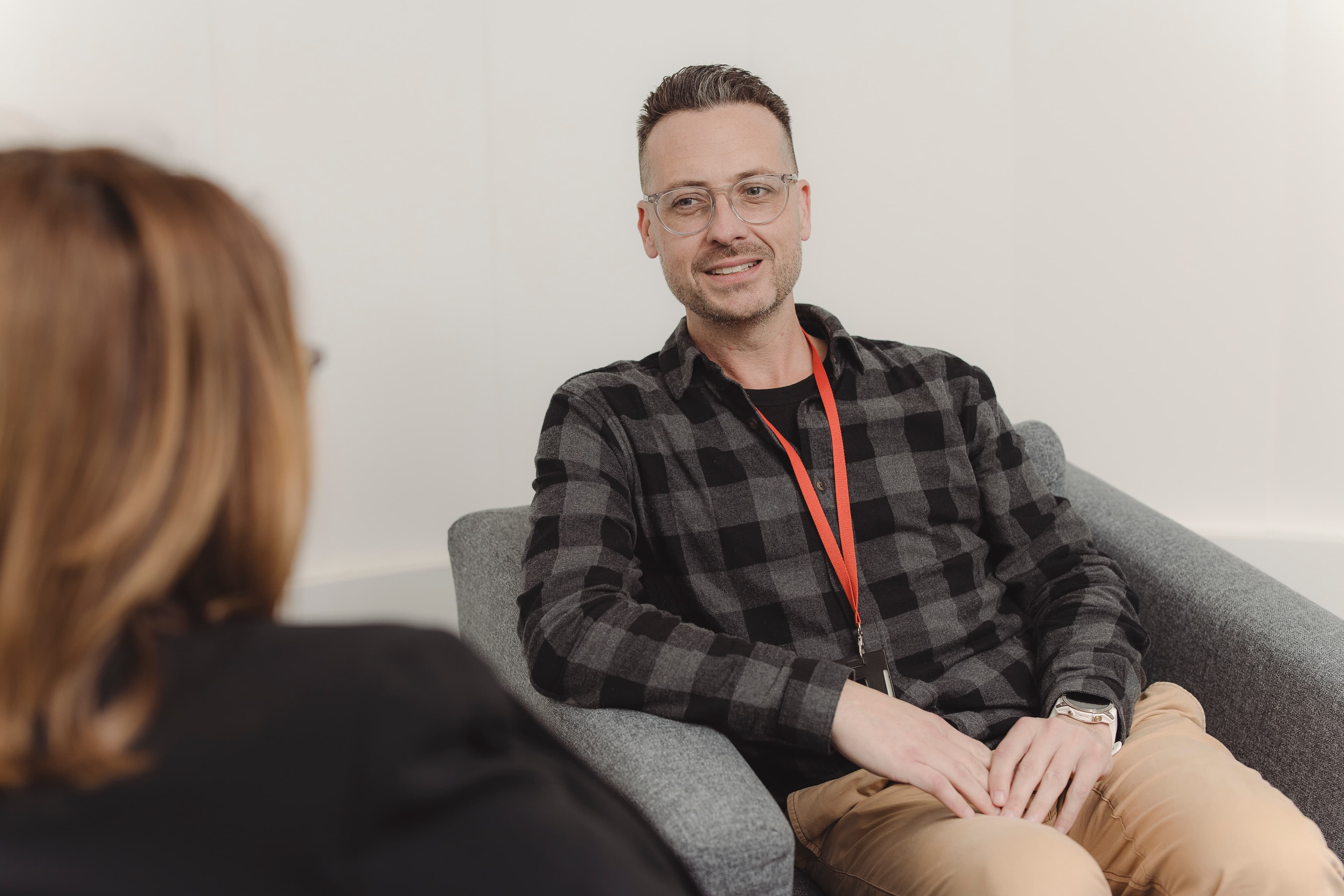 A man seated on a chair having a conversation with a woman.