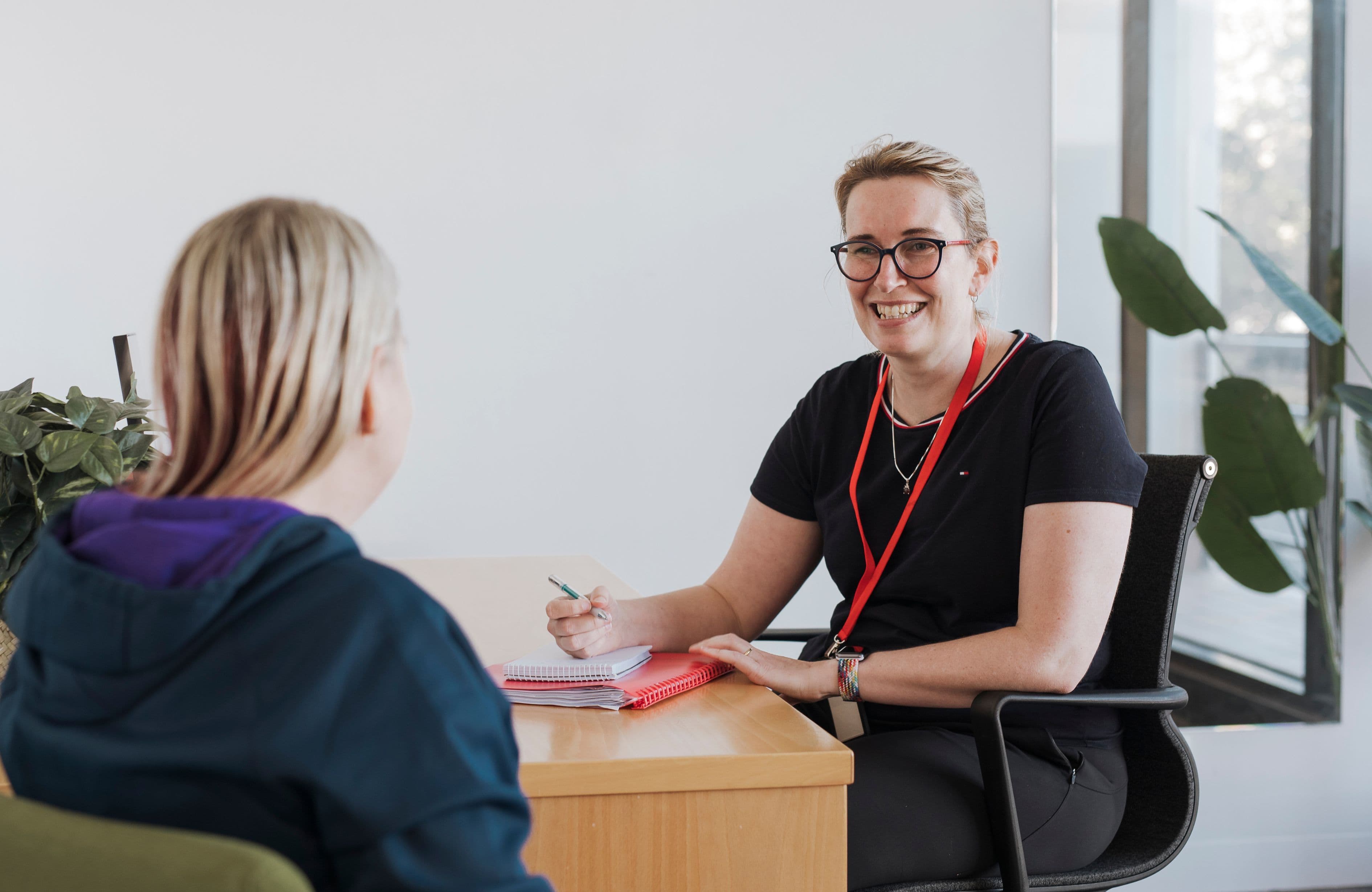 An MS Plus staff member seated at a desk opposite a client of MS Plus doing a consultation.