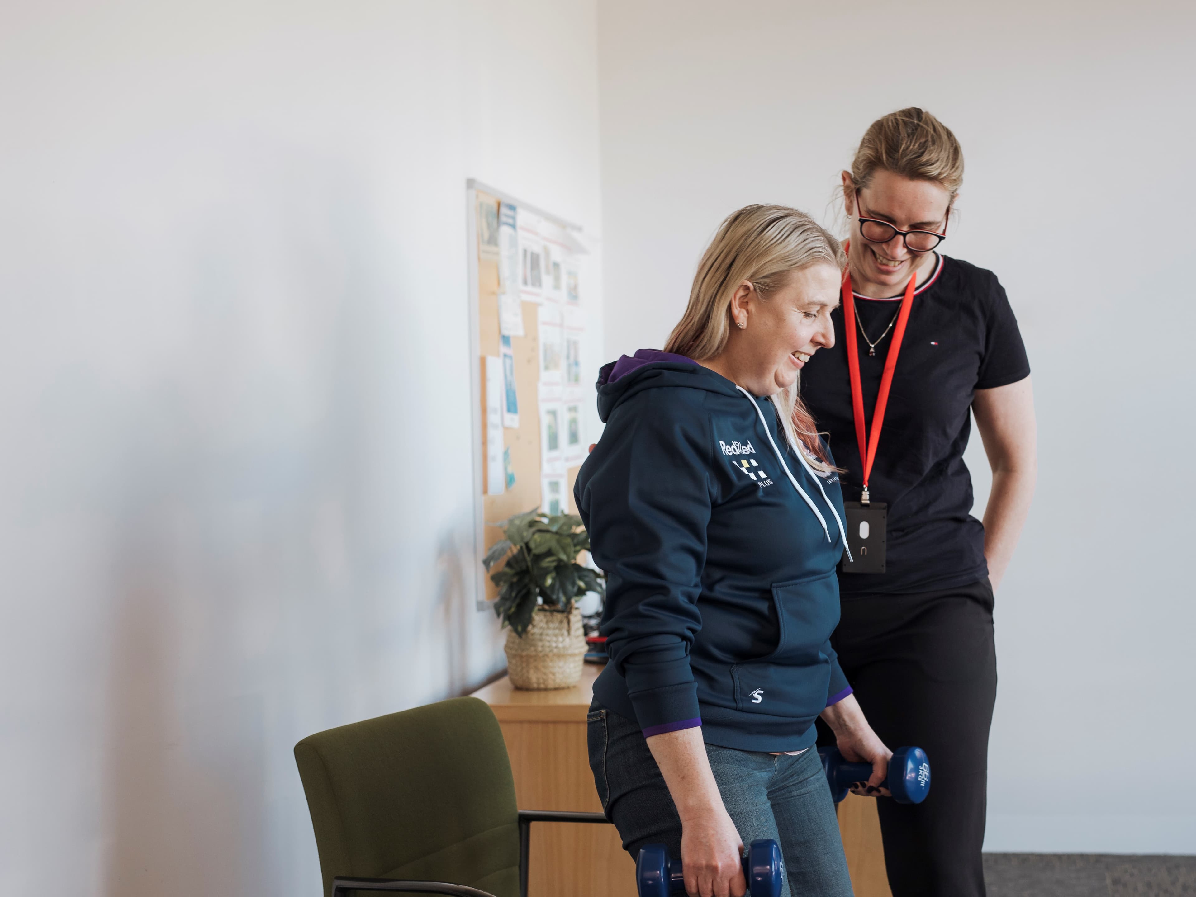 physiotherapist stands next to client holding weights 2