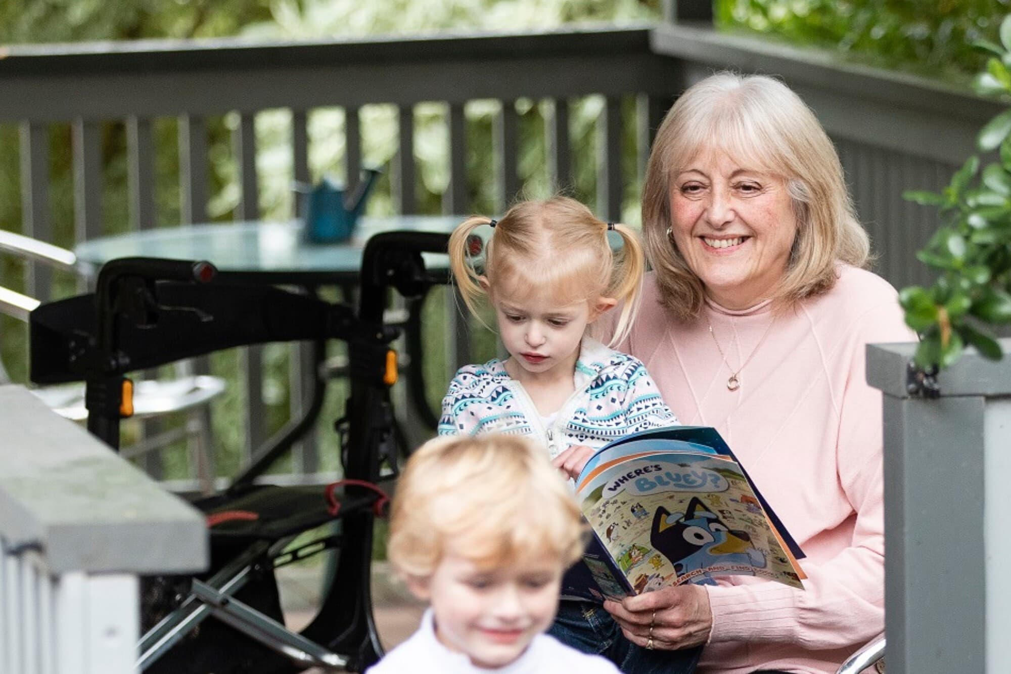 An old woman smiling and reading book to two yound chilkdren, a girl and a boy