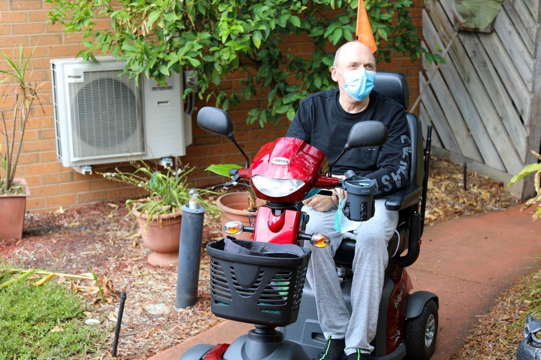 A man seated in a powered wheelchair outdoors in a garden.