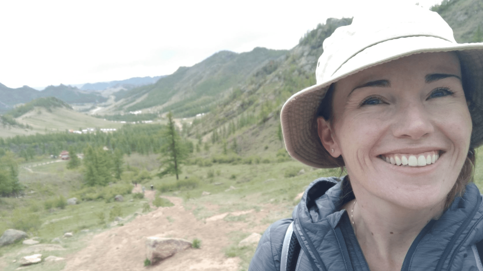 Eliza smiles at camera while standing in hilly outdoor area