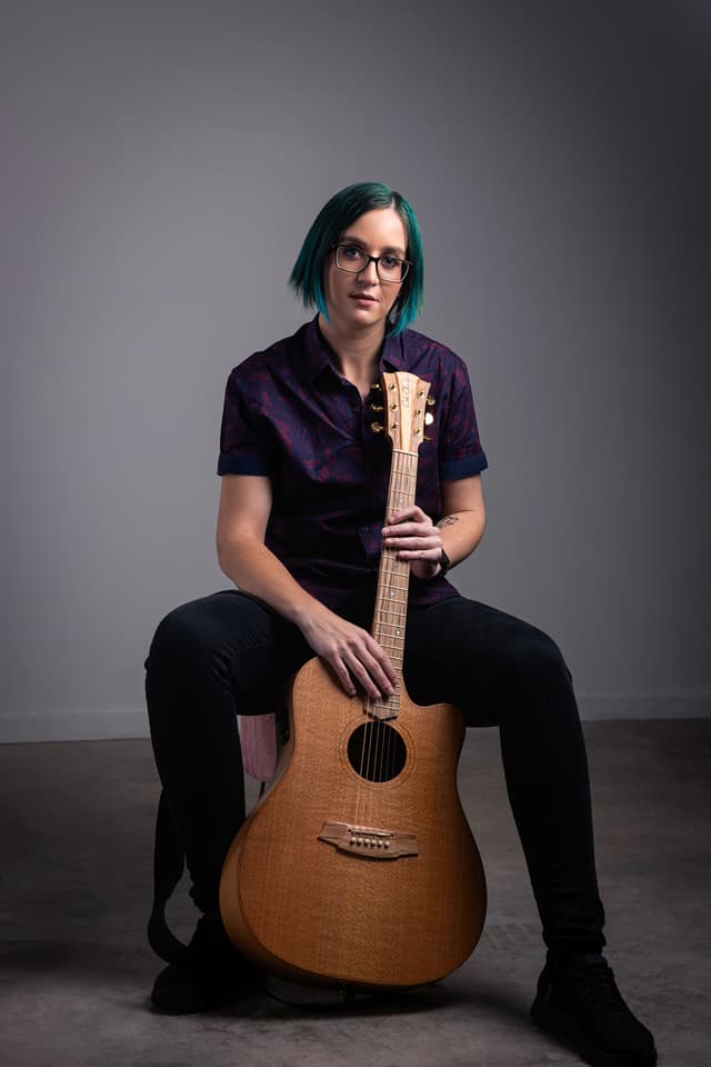 Jemma is seated and holding a guitar