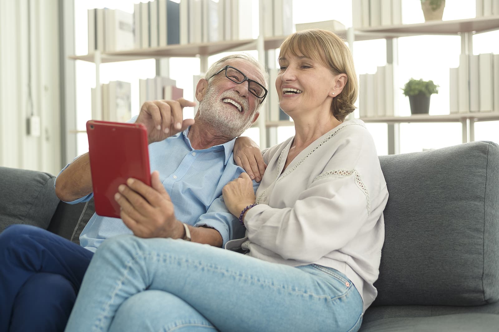 A senior man and woman seated on a couch sharing a digital tablet device.